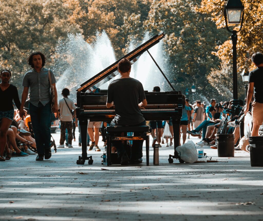 Person plays a piano in the middle of a public park, with a backdrop of water fountains