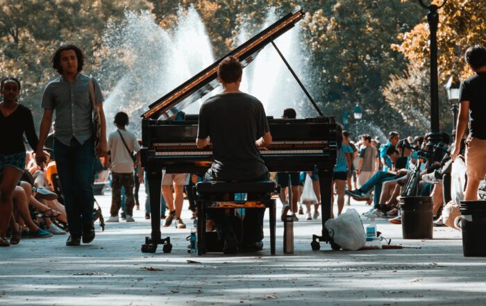 Person plays a piano in the middle of a public park, with a backdrop of water fountains